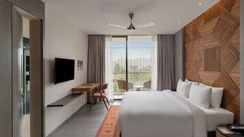 A modern hotel room with a large bed, a desk, a chair, a TV, and a balcony with curtains.