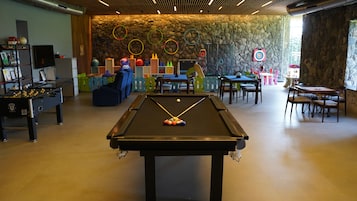 A pool table with colorful balls, a foosball table, and a dartboard in a room with stone walls and a wooden ceiling.