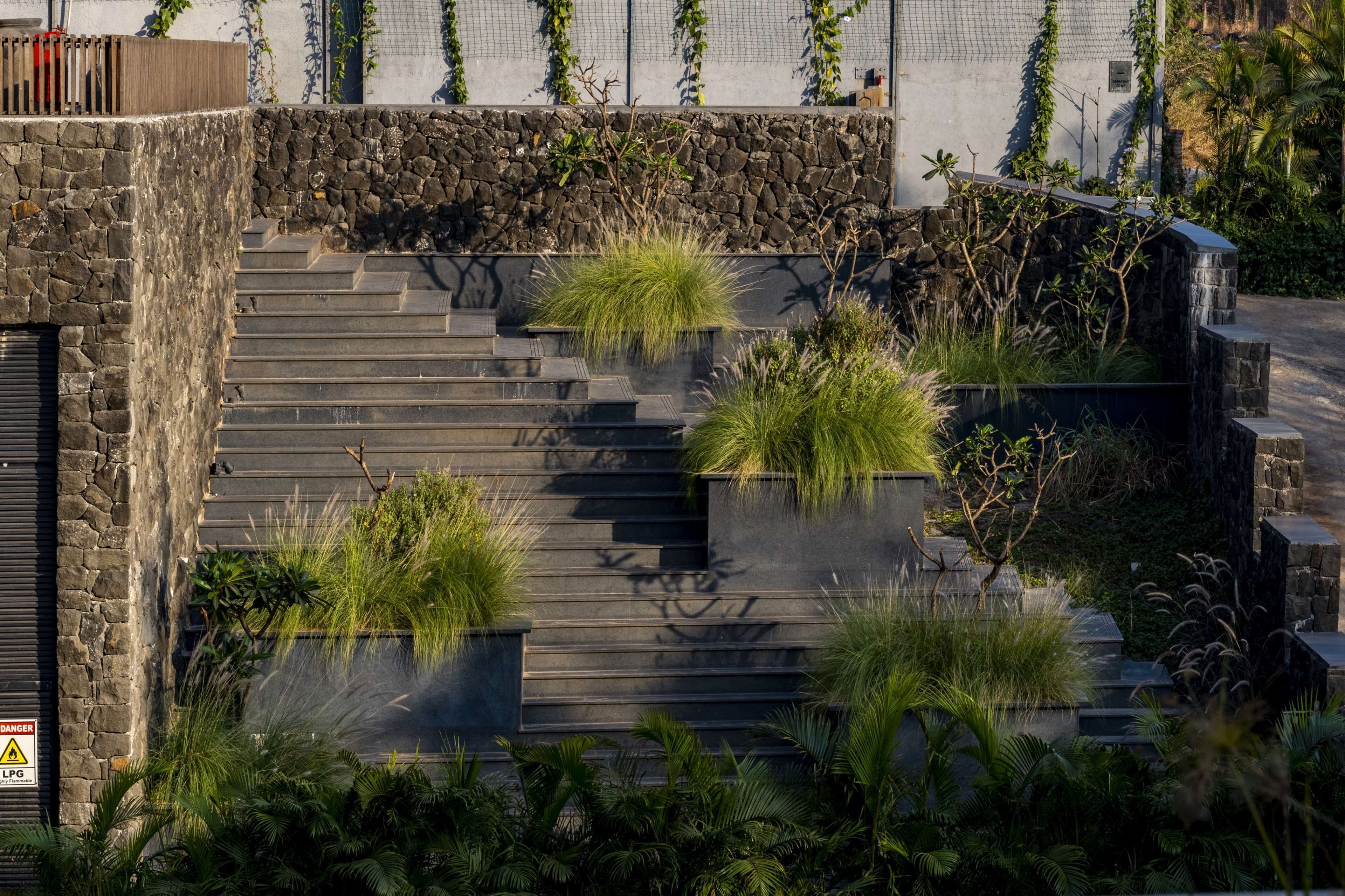 A modern building with stone steps, green plants, and a warning sign.