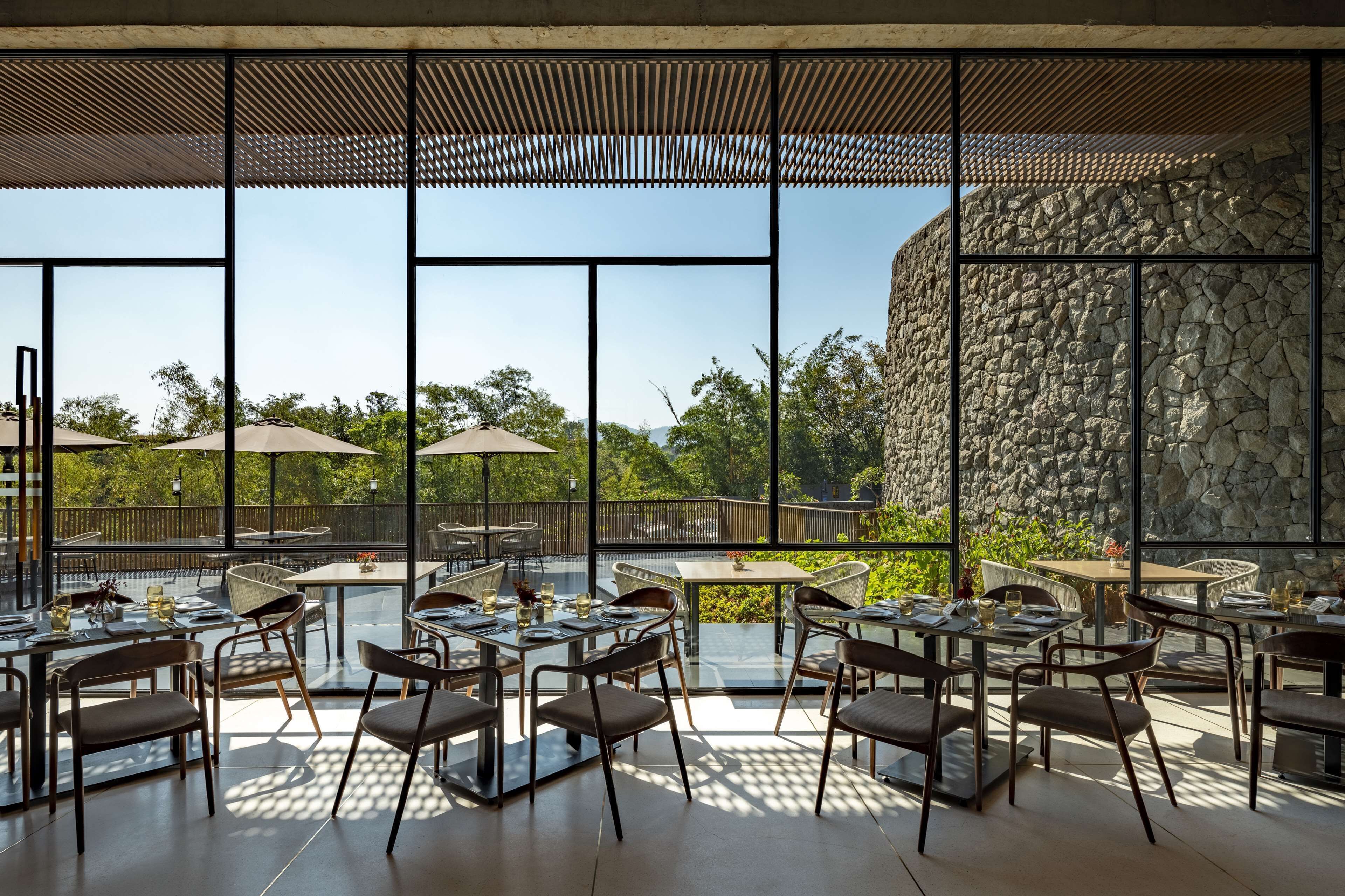 An outdoor dining area with tables and chairs, large windows, and a stone wall.