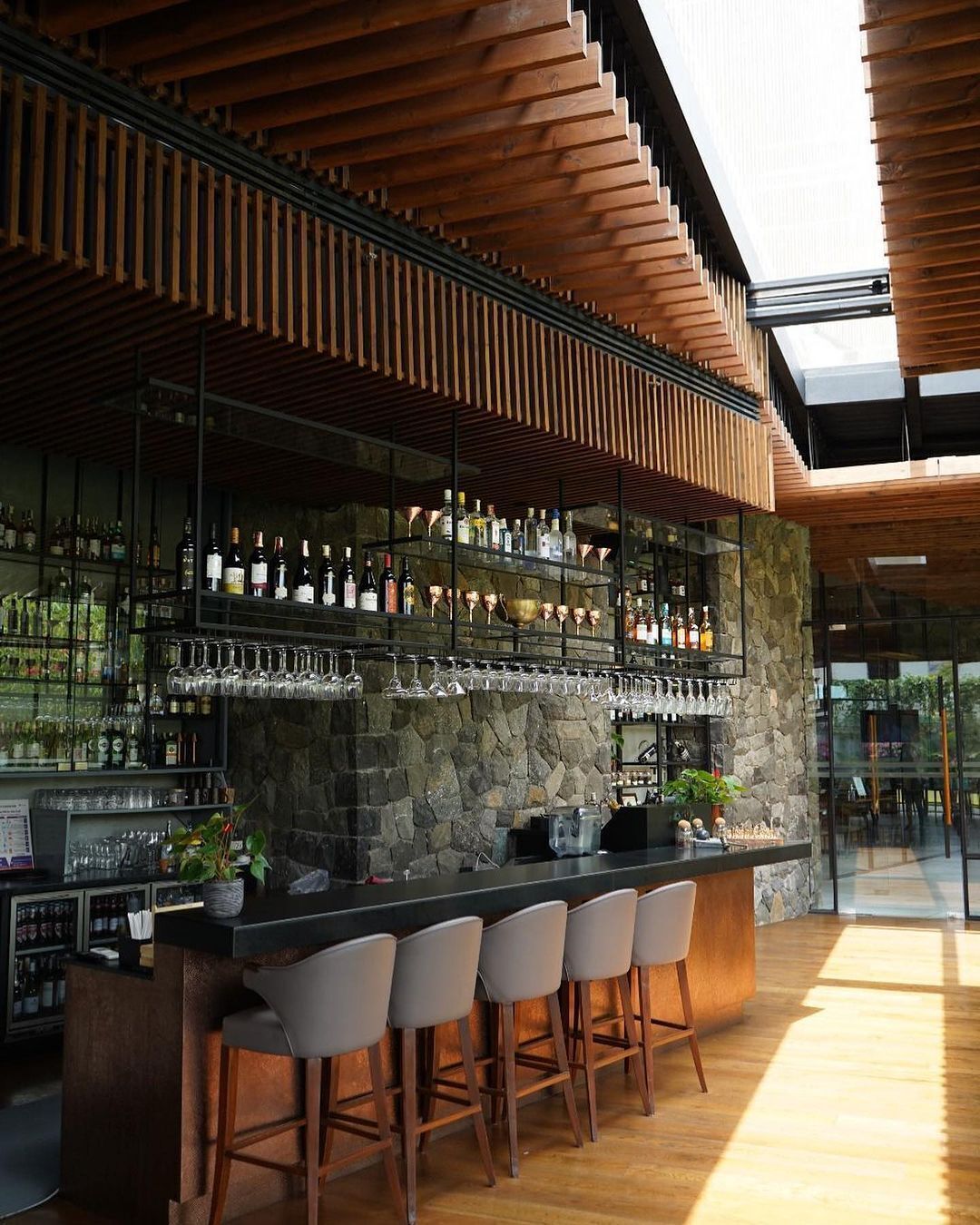 A modern bar with a stone wall, wooden ceiling, and bar stools.