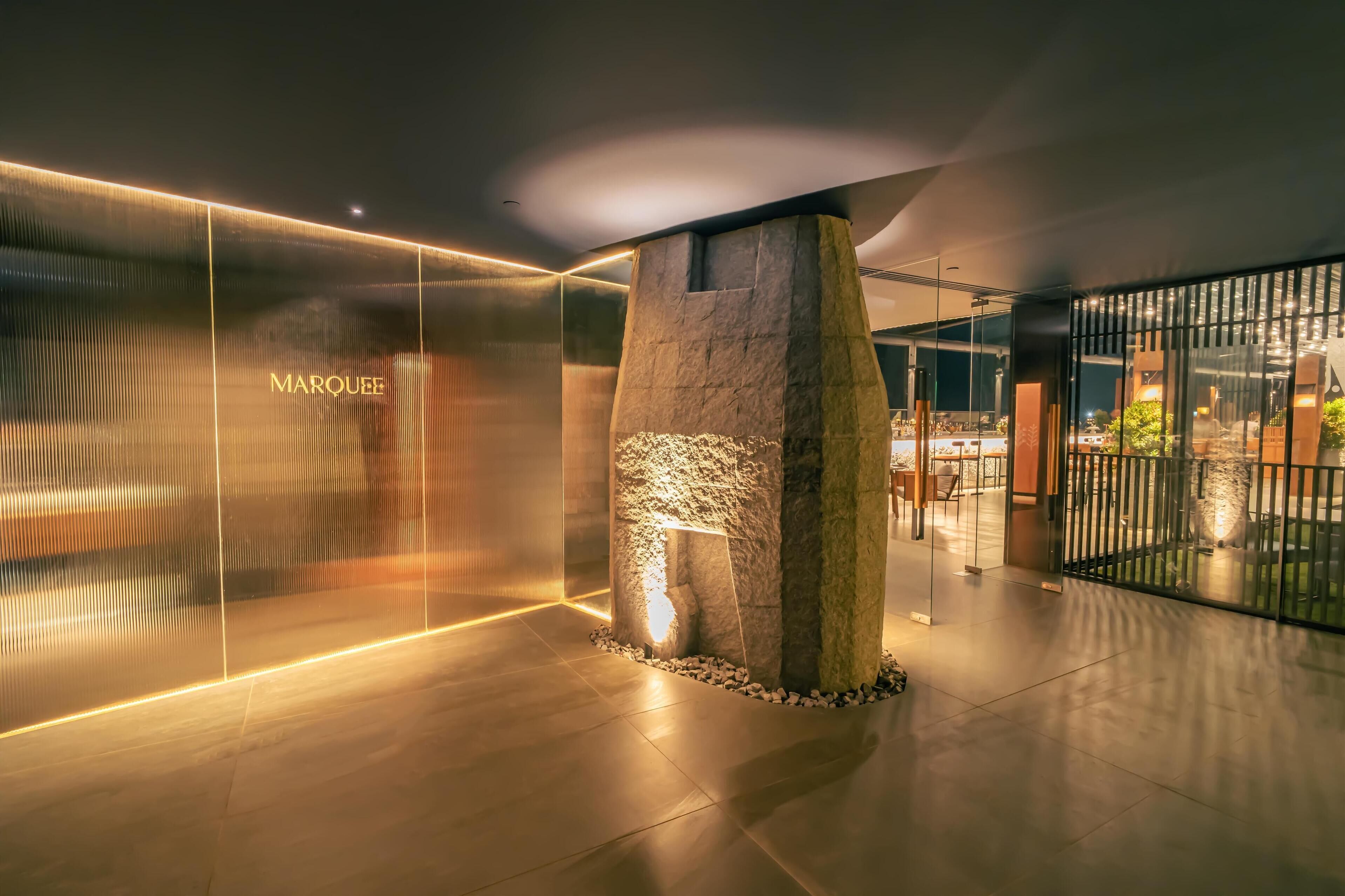A modern interior with a stone column, a glass wall with 'MARQUEE' signage, and a well-lit reception area.