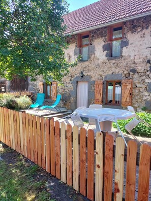 Una casa de piedra con techo de tejas, cerca de madera y mobiliario exterior.