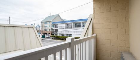 A balcony with a white railing, beige brick wall, and a view of a building with multiple floors and a blue roof.