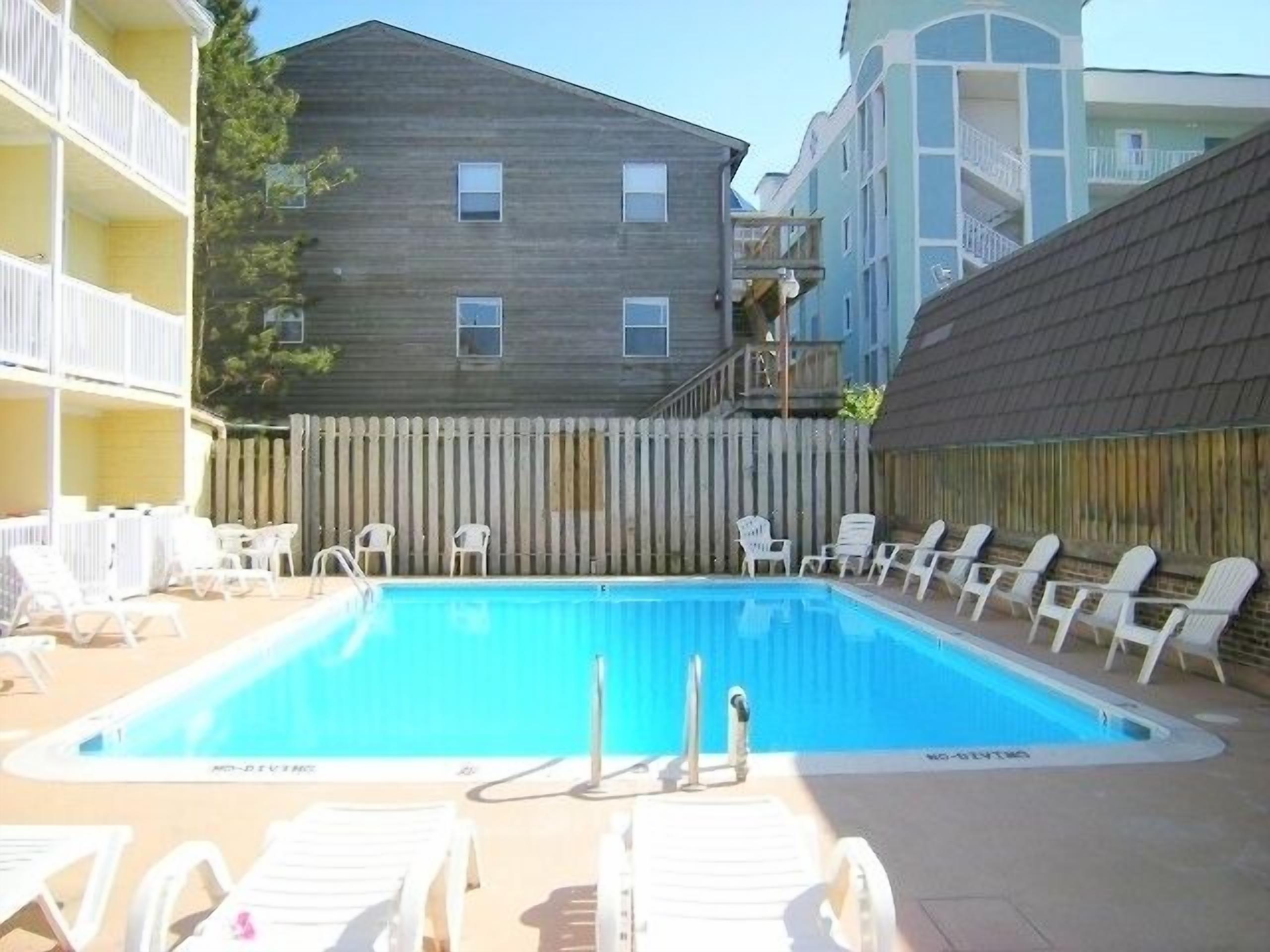 A rectangular swimming pool with lounge chairs and a wooden fence.