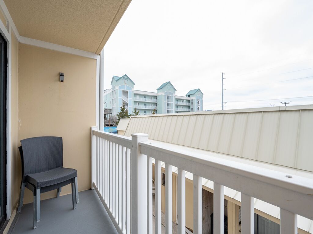 A balcony with a chair, a railing, and a view of a building with multiple stories and a blue roof.