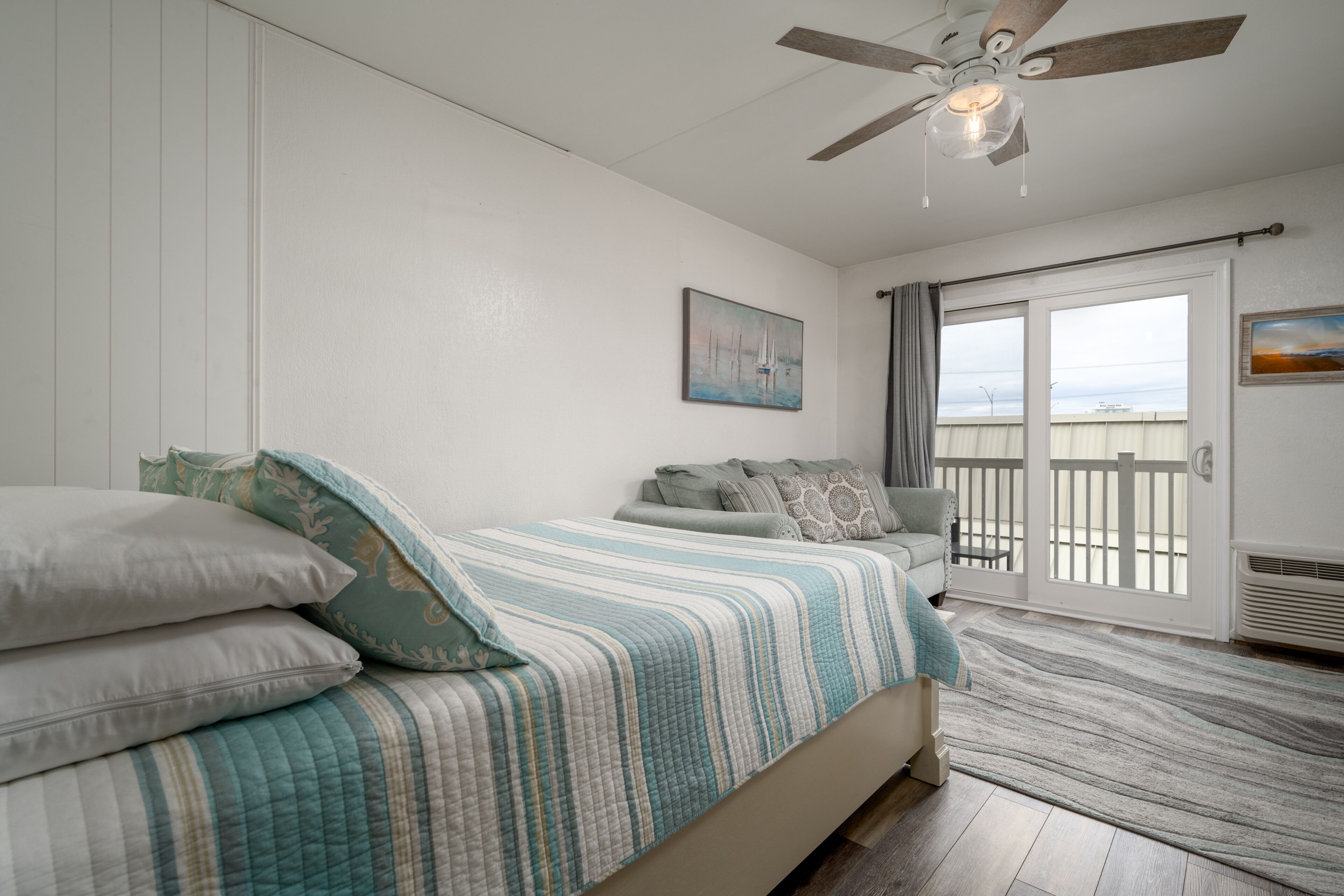 Une chambre à coucher avec un lit, un ventilateur de plafond, une fenêtre donnant sur un beau paysage et une porte menant à un balcon.