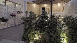 Een binnenplaats met een overdekte zithoek, planten in potten en een stenen muur.