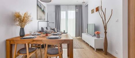 A modern living room with a dining area, a sofa, a TV, and a wooden dining table with chairs.
