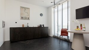 Une cuisine moderne avec des meubles de couleur sombre, un plan de travail blanc et un coin repas comprenant une table ronde et une chaise rouge.
