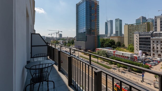 Un balcon avec une table et des chaises, donnant sur un paysage urbain composé d’immeubles modernes et d’une grue de construction.