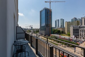 A balcony with a table and chairs, overlooking a cityscape with modern buildings and a construction crane. - Warsaw | Marszałkowska 140 | Modern Studio | Air-conditioning and Balcony (Warszawa)