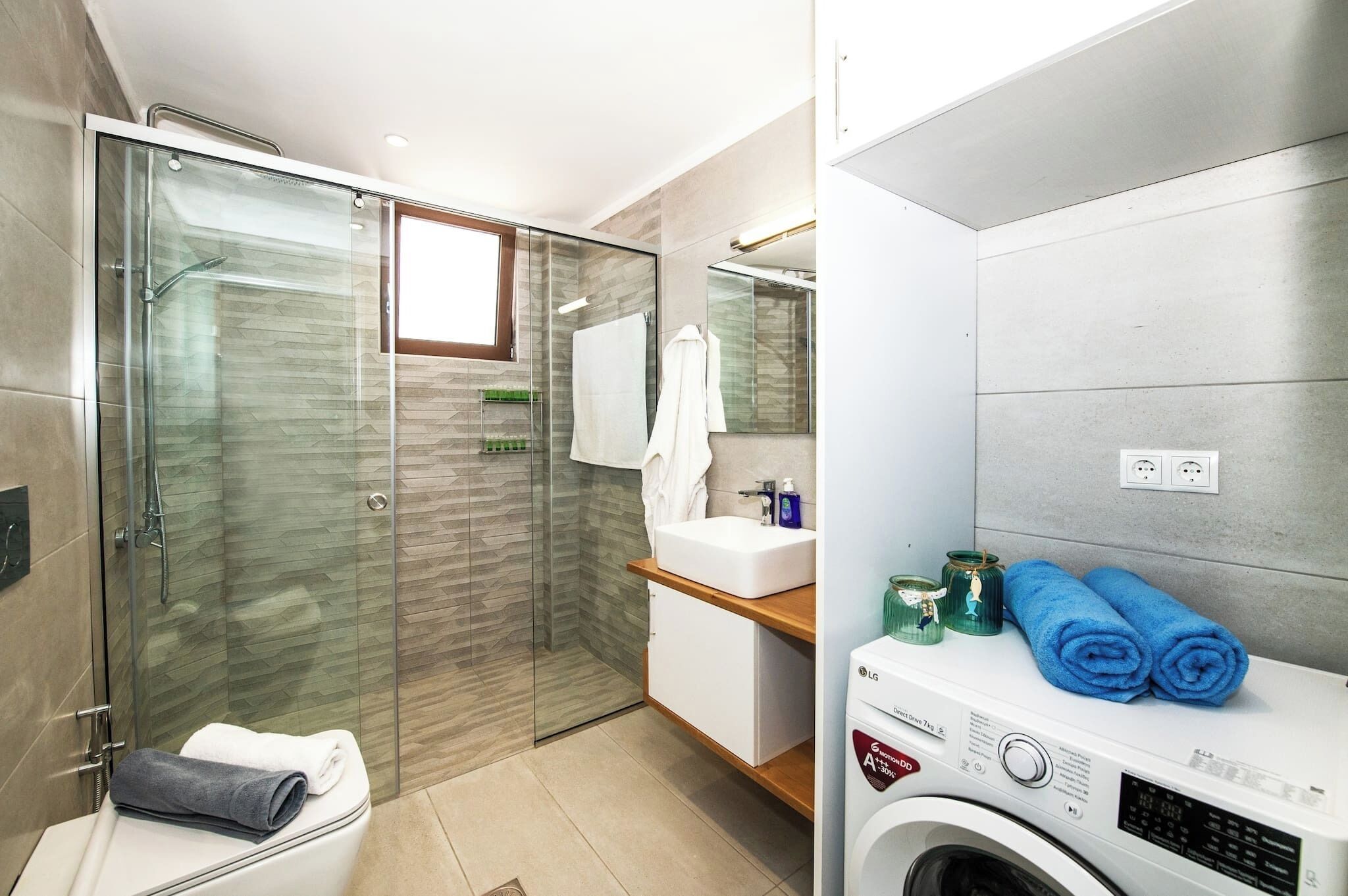 Une salle de bain moderne avec une douche à parois de verre, un lavabo blanc et un lave-linge encastré.