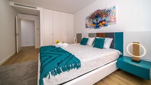 Un dormitorio moderno con una cama, ropa de cama verde azulado y blanca, un cuadro abstracto colorido y una mesita de noche con luz de aro.