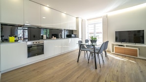 Una cocina moderna con armarios blancos, un comedor con mesa y sillas, y un televisor en la pared.