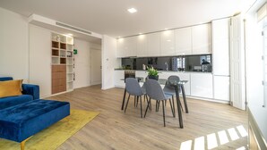 Una sala de estar moderna con un sofá azul, una mesa de comedor con sillas y una cocina con armarios y electrodomésticos blancos.