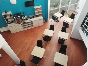 A modern room with wooden flooring, a blue accent wall, and a TV mounted on the wall. There are several tables and chairs arranged for dining or working. - Hotel Mervil Airport (Merville)