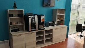 A reception area with a coffee machine, microwave, and a small TV on the wall. - Hotel Mervil Airport (Merville)