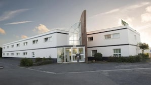 A modern hotel with a glass entrance, a prominent vertical structure, and a sign indicating it is a hotel. - Hotel Mervil Airport (Merville)