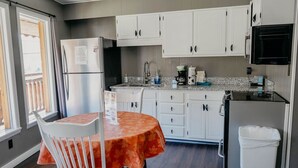 A compact kitchen with white cabinets, a stainless steel refrigerator, a granite countertop, and a dining table with a patterned tablecloth.