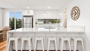 A modern kitchen with white cabinetry, a stainless steel refrigerator, a large island with bar stools, and a decorative wall clock. - Sunrise Mansion with Pool - 6 bedrooms (KINGSCLIFF)