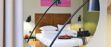 A circular mirror reflecting a modern bedroom with a wooden headboard, white bedding, a red teapot, and a black handbag.