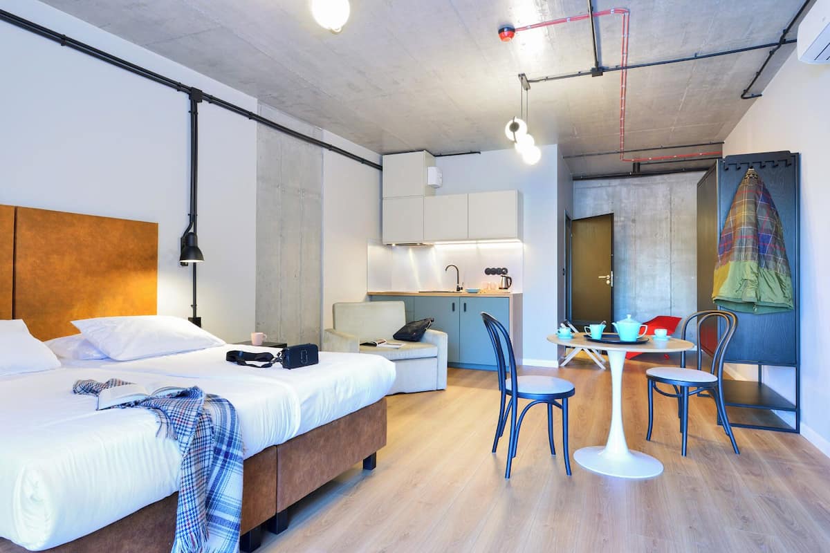 Quarto de hotel moderno com uma cama grande, uma escrivaninha e uma cozinha compacta.