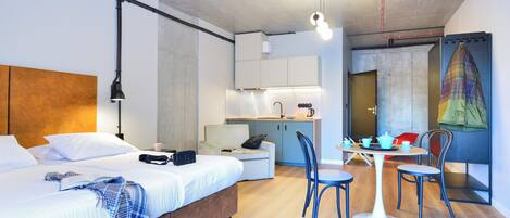 Una habitación de hotel moderna con cama, mesita de noche y una kitchenette pequeña.