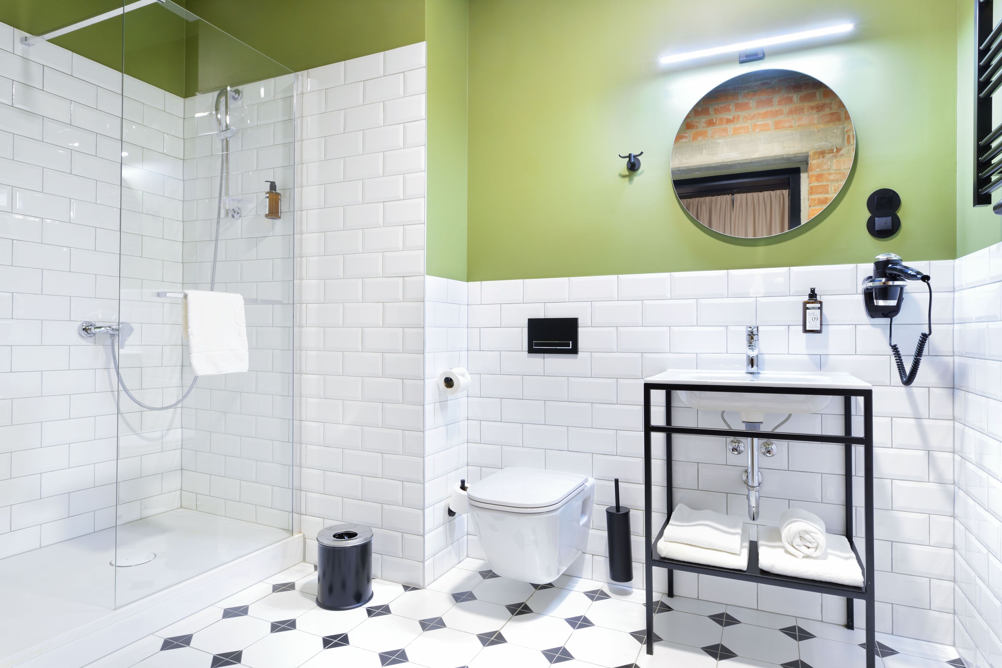A bathroom with a glass shower enclosure, a white toilet, a sink with a black frame, and a mirror on the wall.