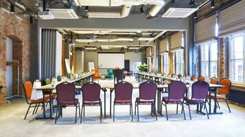 A conference room with long tables and chairs, large windows, and exposed brick walls.