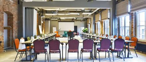 A conference room with long tables and chairs, large windows, and exposed brick walls.