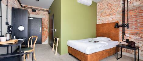 Een moderne hotelkamer met een bakstenen muur, een bed met wit beddengoed, een bureau met stoel en een kleine tafel met lamp.