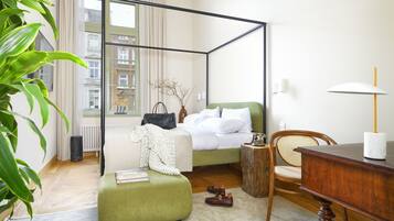 A four-poster bed with a green upholstered headboard, a wooden nightstand, a wicker chair, and a desk with a lamp.