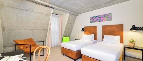 A hotel room with two beds, a desk, a chair, a small table with a lamp, and a painting on the wall.