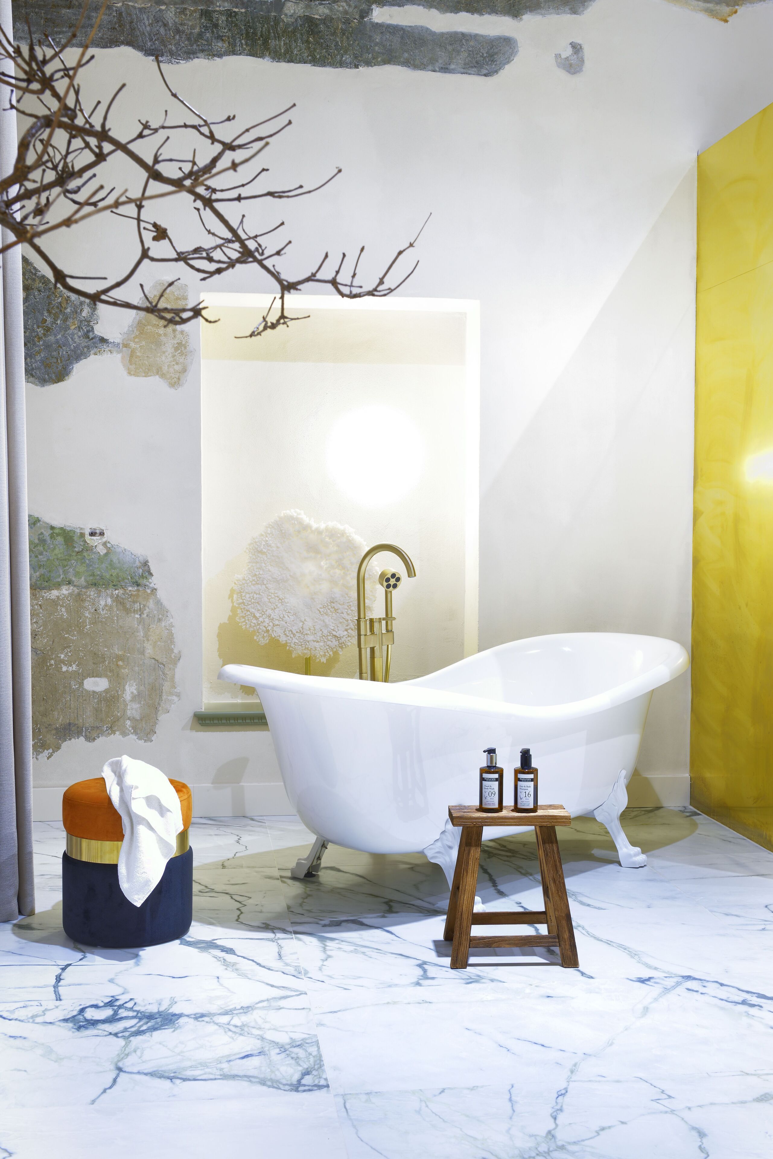 A bathroom with a freestanding bathtub, a wooden stool with bottles, and a towel on a chair.