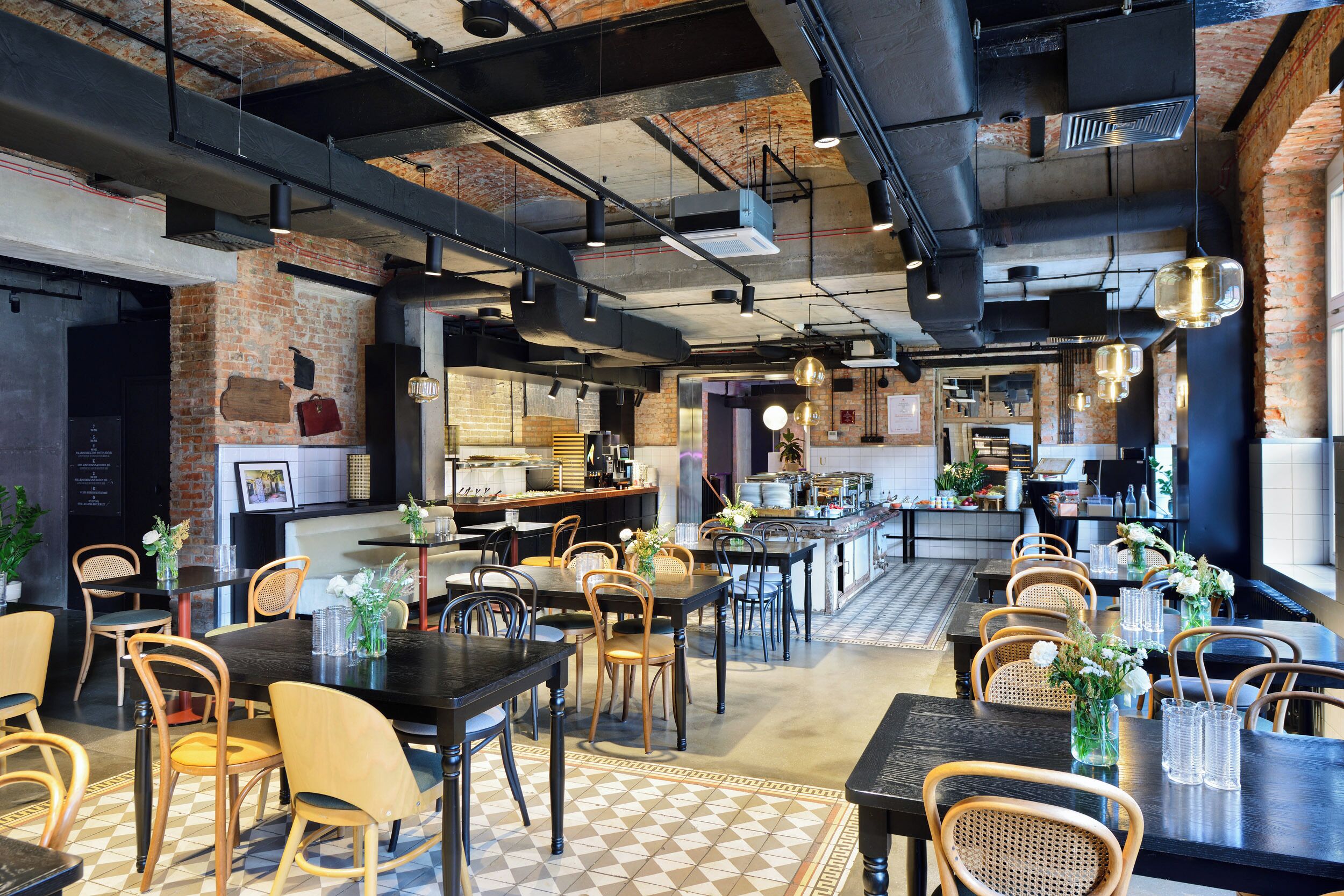 A modern restaurant with exposed brick walls, industrial ceiling pipes, and a mix of wooden and metal furniture.