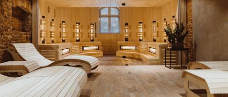 A spa room with wooden benches and massage tables, a brick floor, and a large window with a view.