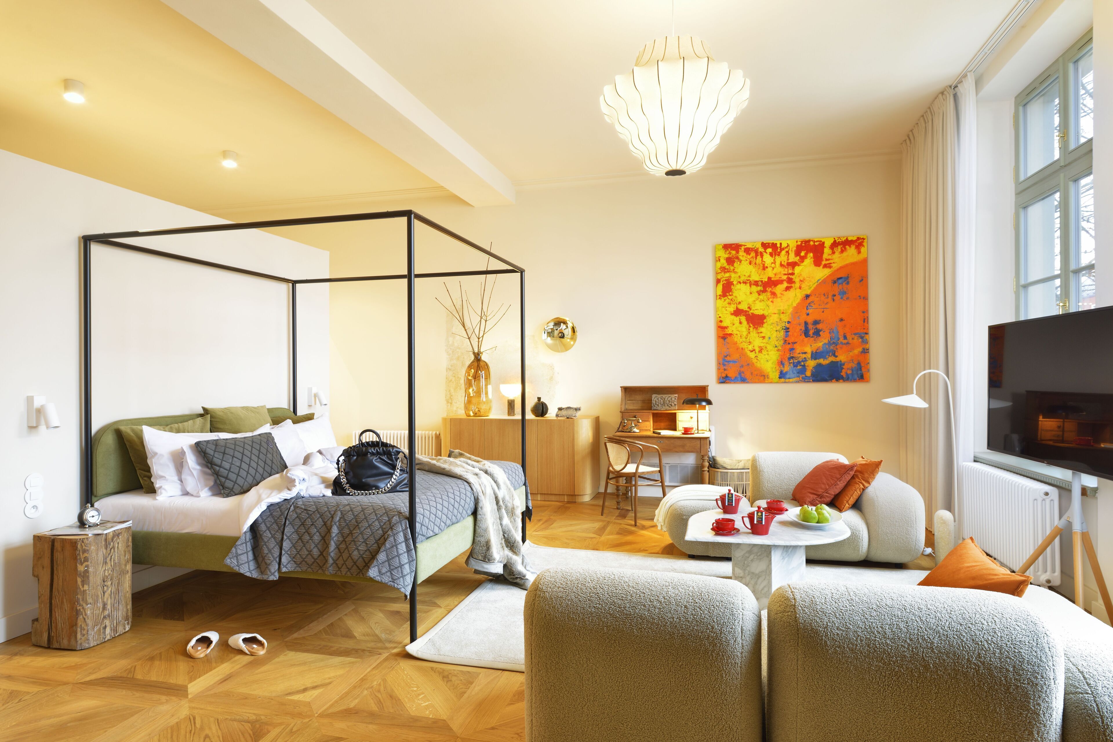 Ett modernt hotellrum med en säng med himmelssäng, en soffa, en matplats och ett stort fönster.