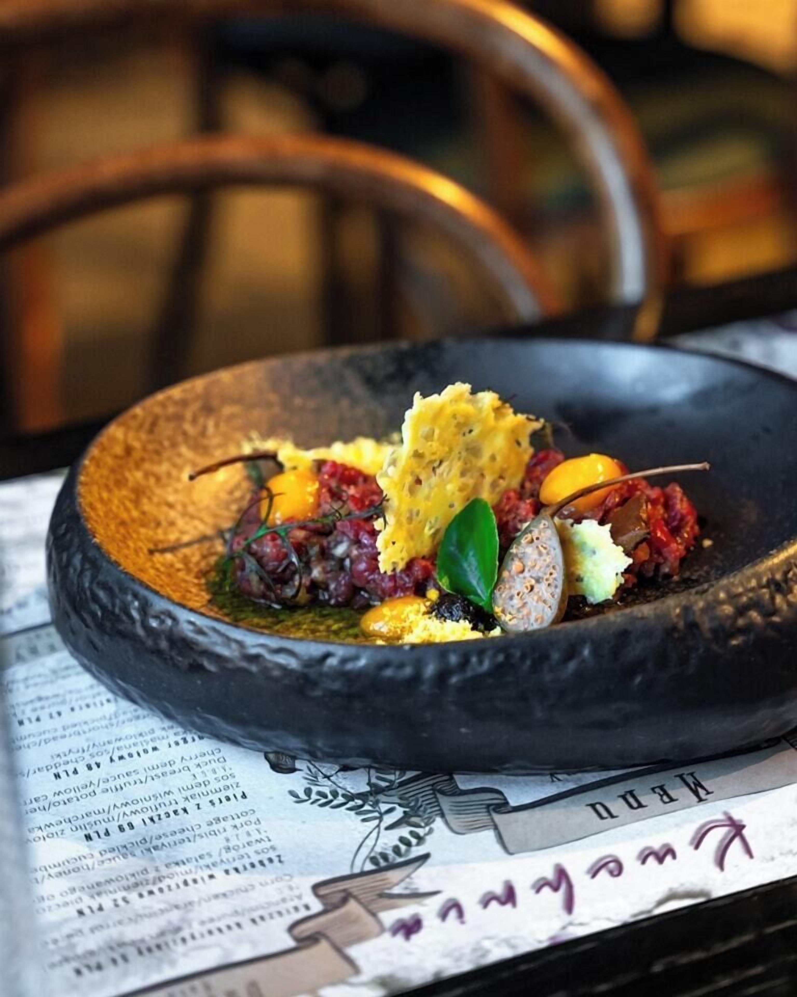 A dish with various ingredients on a black plate, placed on a table with a newspaper underneath.