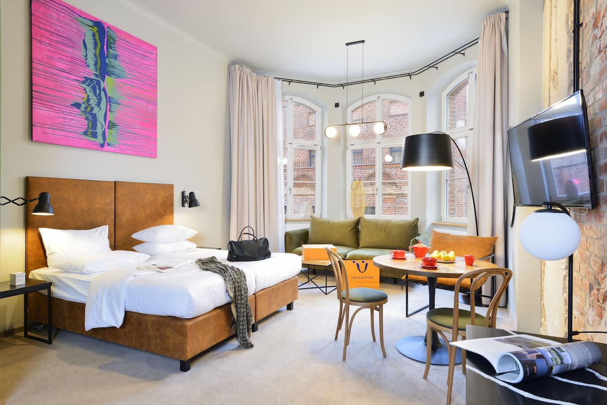 Quarto de hotel com cama, escrivaninha, cadeira, sofá e televisão.