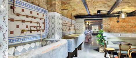 Un restaurante con paredes de ladrillo visto, paredes alicatadas con diseños geométricos y una larga barra con taburetes.