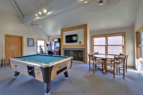 Une table de billard avec une cheminée, un téléviseur fixé au-dessus, et un coin repas avec des chaises.
