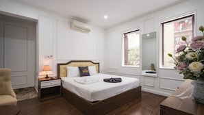 Un dormitorio ordenado con cama, mesita de noche, lámpara y un jarrón de flores.