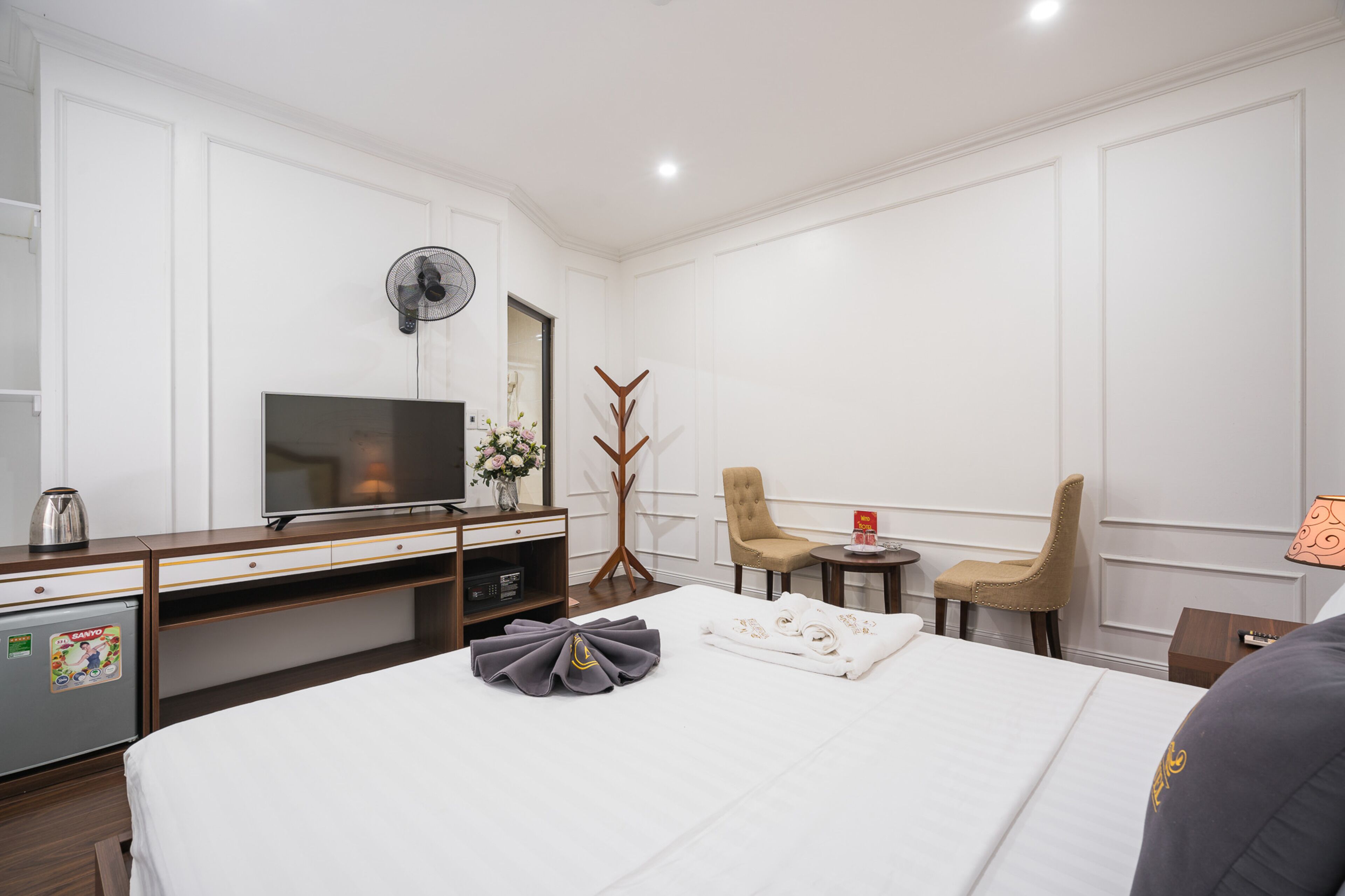 A hotel room with a bed, a TV, a desk, a chair, a small table, and a coat stand.