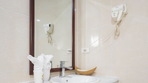 Un baño con un espejo grande, un lavamanos, un secador de pelo y un dispensador de toallas.