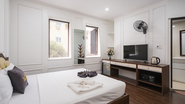Una habitación de hotel con una cama grande, televisión, escritorio con computadora y ventana con vista a edificios.