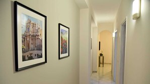 A hallway with two framed pictures on the wall, a small table with a lamp, and a door at the end. - Casa Vacanze le Palme Netine (Noto)