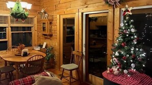 Un intérieur en bois avec une table à manger, des chaises, un sapin de Noël et une cheminée.