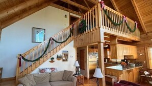 L’intérieur chaleureux d’un chalet avec un escalier en bois, un salon doté d’un canapé et d’une lampe, et un coin cuisine.
