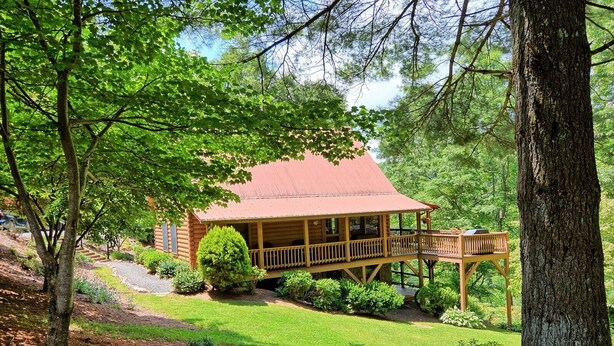 Une cabane en bois dotée d’un porche, entourée d’arbres et d’une pelouse bien entretenue.